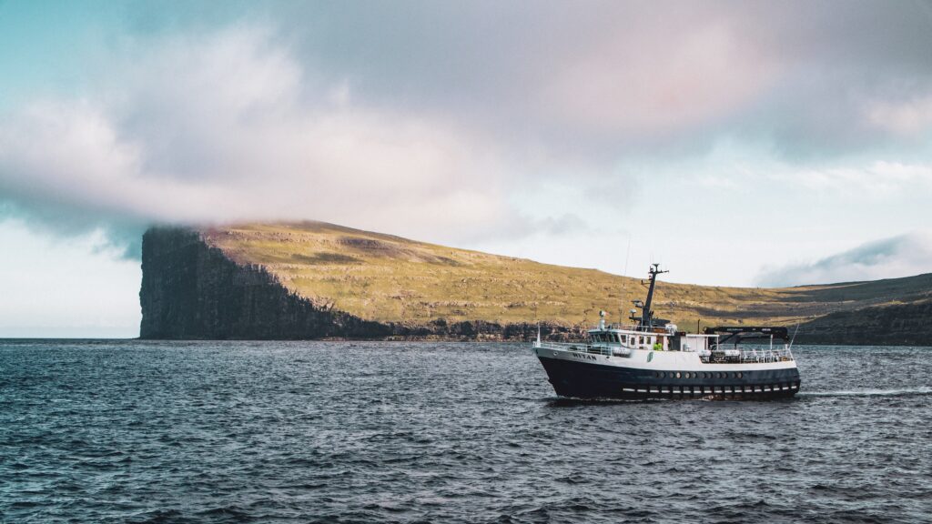 photo of Fugloy Island in the background in front of which a yacht with tourists is sailing