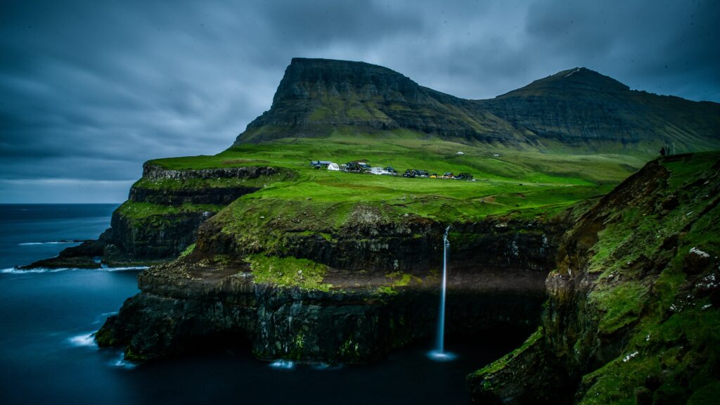 photo of an amazing view of a cliff in the greenery around the water in Gasadalur village, one of the most touristy places in the Faroe Islands