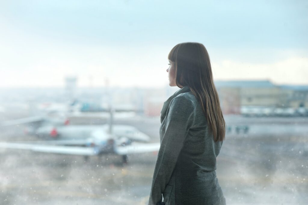 photo of a girl at the airport in rainy weather looking out the window at the airplane