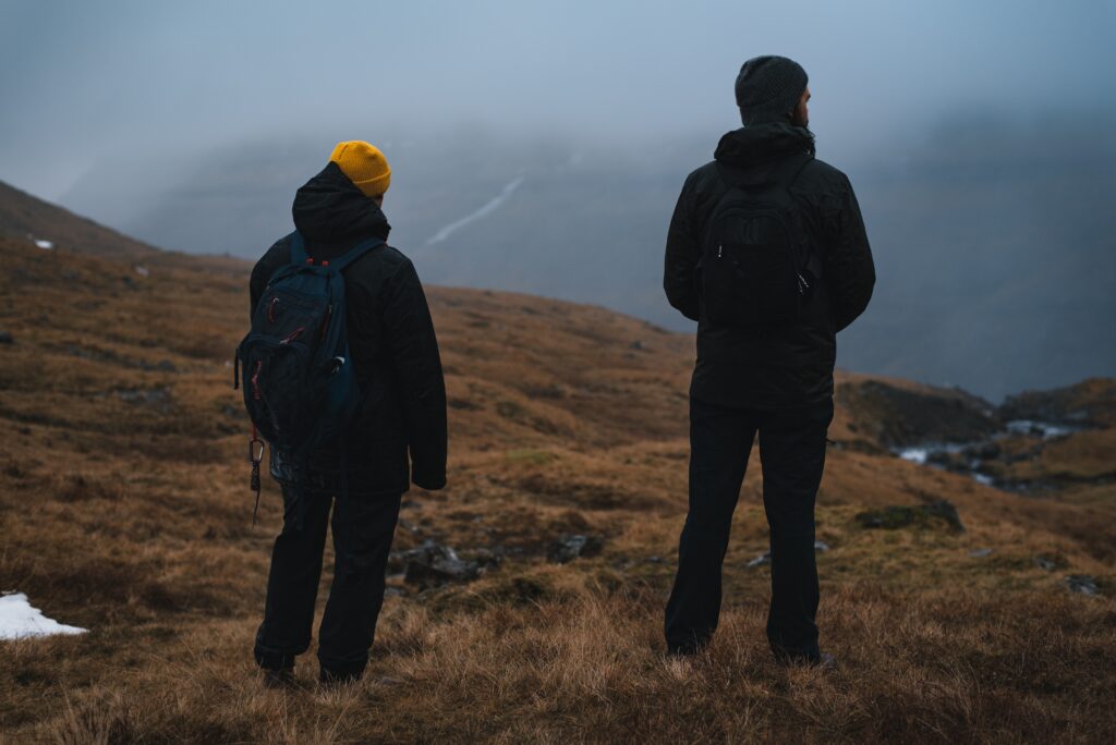 2 warmly dressed men stand on the edge of a cliff in the Faroe Islands