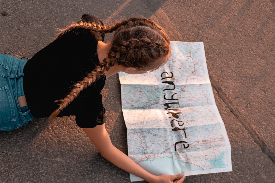 a girl in a black t-shirt with pigtails looks at a map that says "anywhere" in marker.