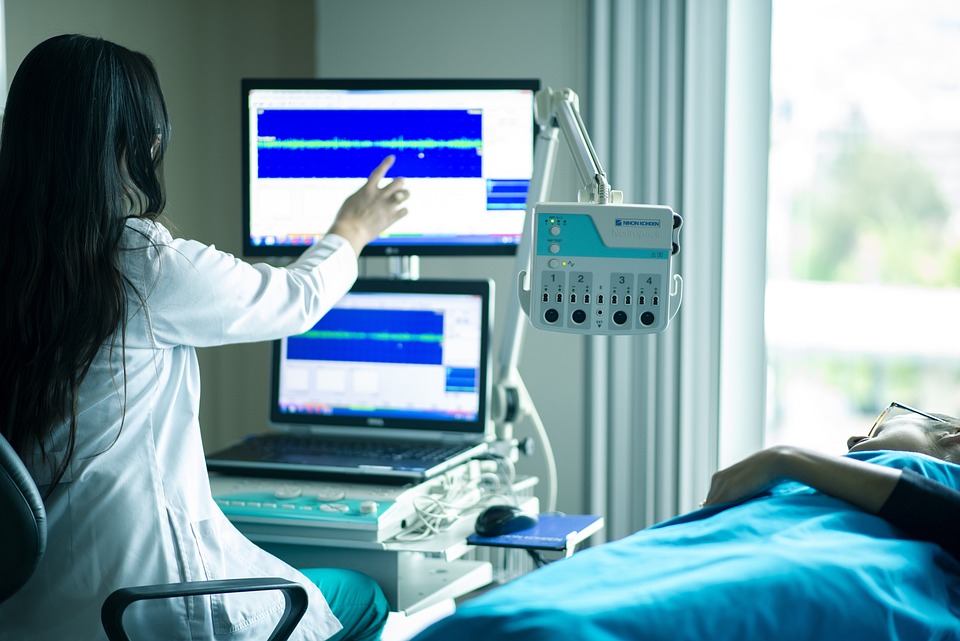 the doctor looks at a graph on the monitor that the machine has displayed while examining the patient lying next to her on the couch