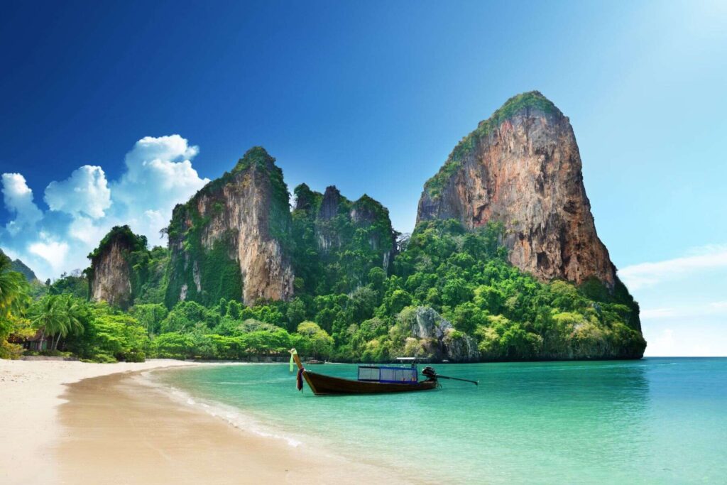A boat moored at Railay Beach with turquoise water in Krabi town in Thailand against the background of an amazing rock in dense vegetation