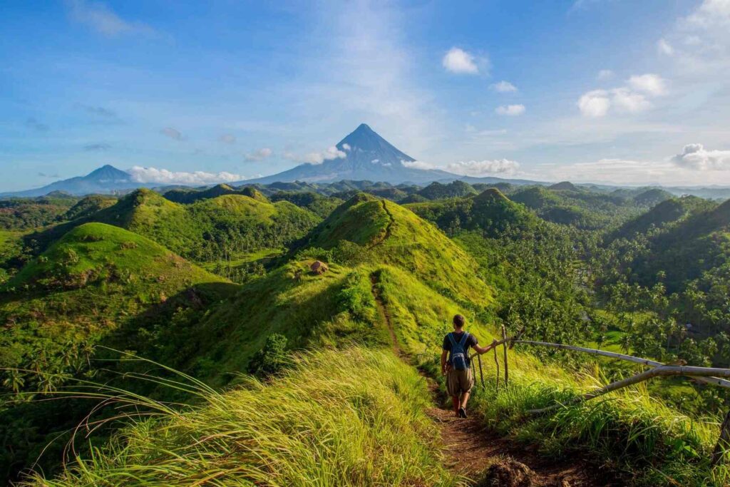 Photo of a man walking along a trail in the green hills towards Mayon Volcano, Quitinday Hills region, Philippines