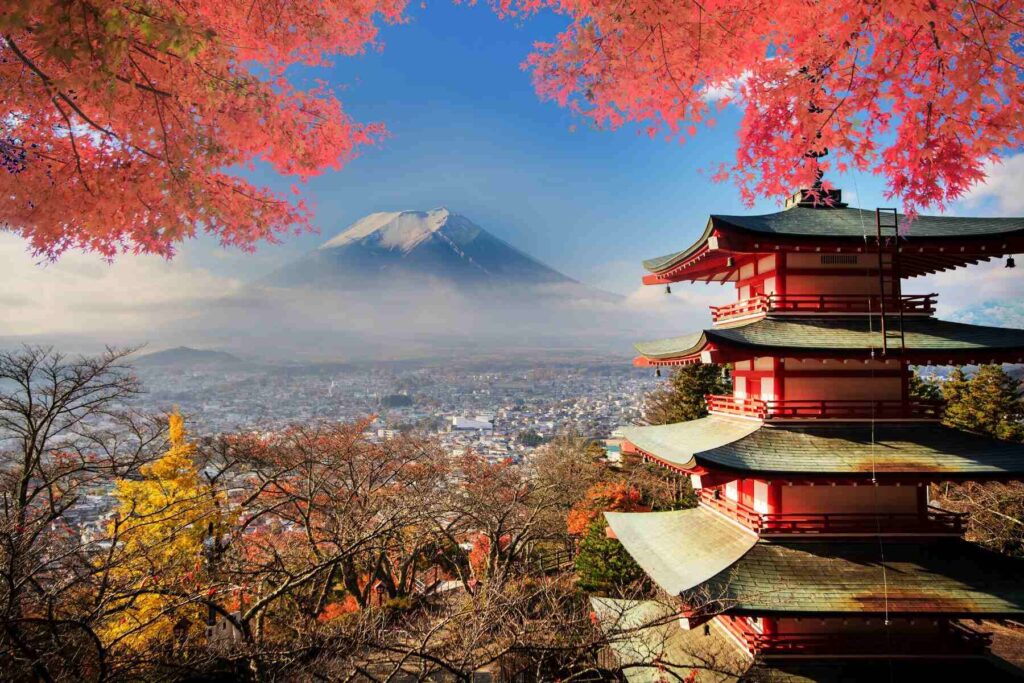 photo of a beautiful view of a classic Japanese building against a background of trees with pink leaves and Mount Fuji in the cloud, Japan