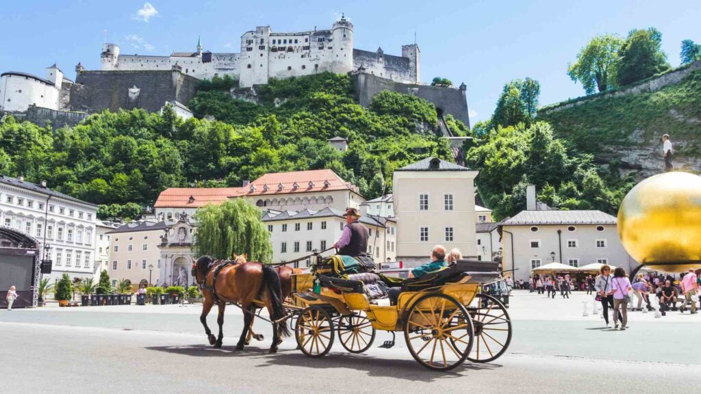 Tourists ride in a horse-drawn carriage in Salzburg, Austria, with a beautiful view of the old architecture in the background