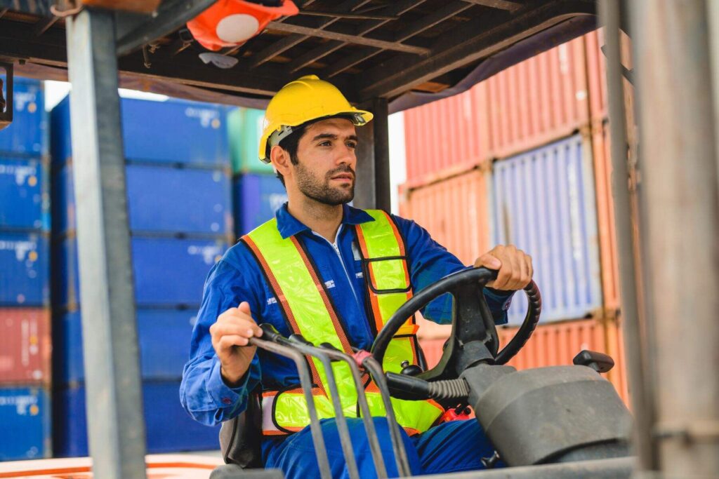 a man in a yellow helmet and a blue uniworm is working abroad on a forklift
