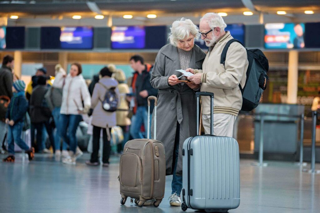 photo of fashionable pensioners at the airport looking at their boarding tickets, with two suitcases next to them